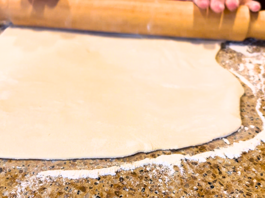 Woman rolling out pierogi dough with a wooden rolling pin