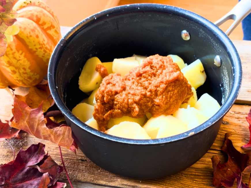 A pot of boiled potatoes with pumpkin puree on top