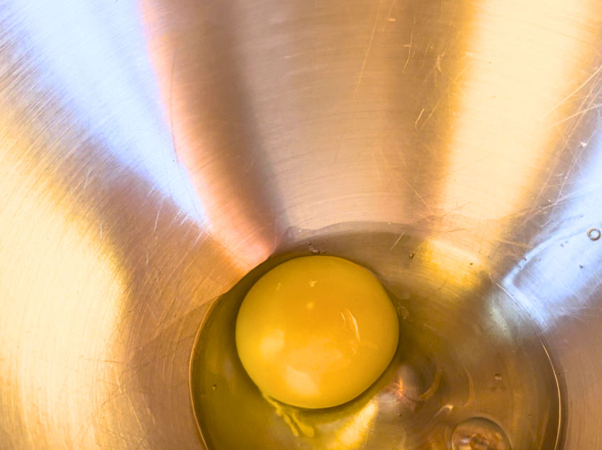 A cracked egg inside a metal bowl