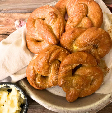 A tray of soft pretzels on top of parchment paper. A small black dish of butter in the foreground.