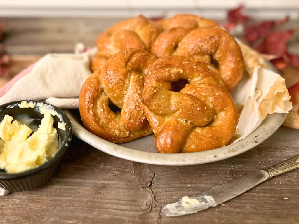 A tin of soft pretzels. A small black dish of butter off to the side and a butter knife in the foreground