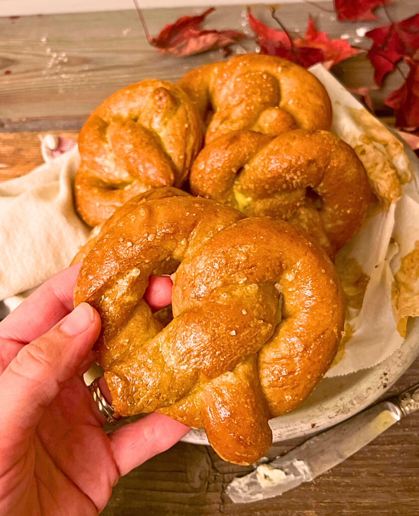 Woman holding a baked pretzel. A metal pan on pretzels in the background