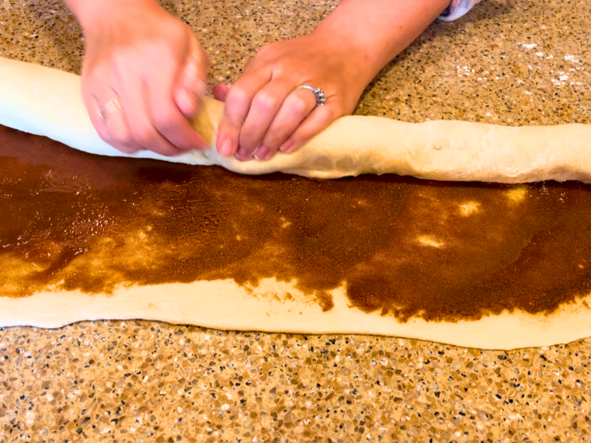 Woman rolling up cinnamon roll dough