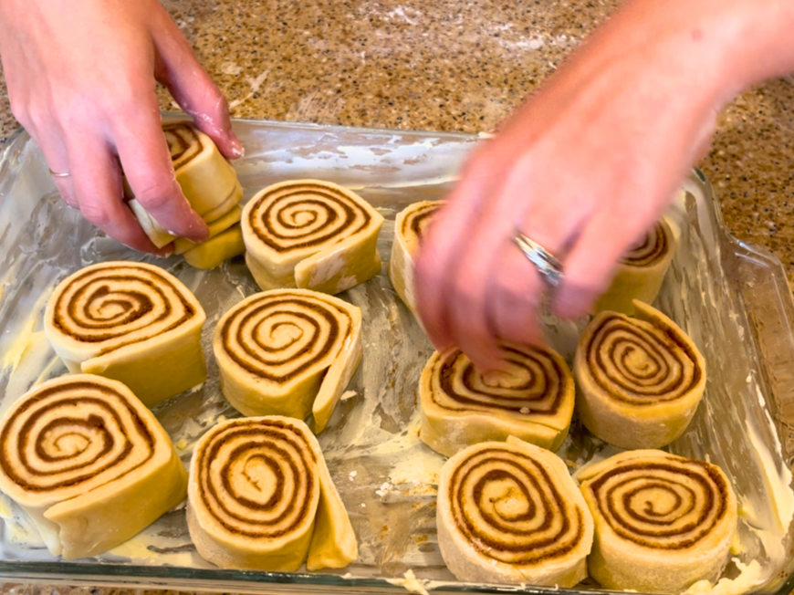 Woman arranging cinnamon roll dough into a greased casserole dish