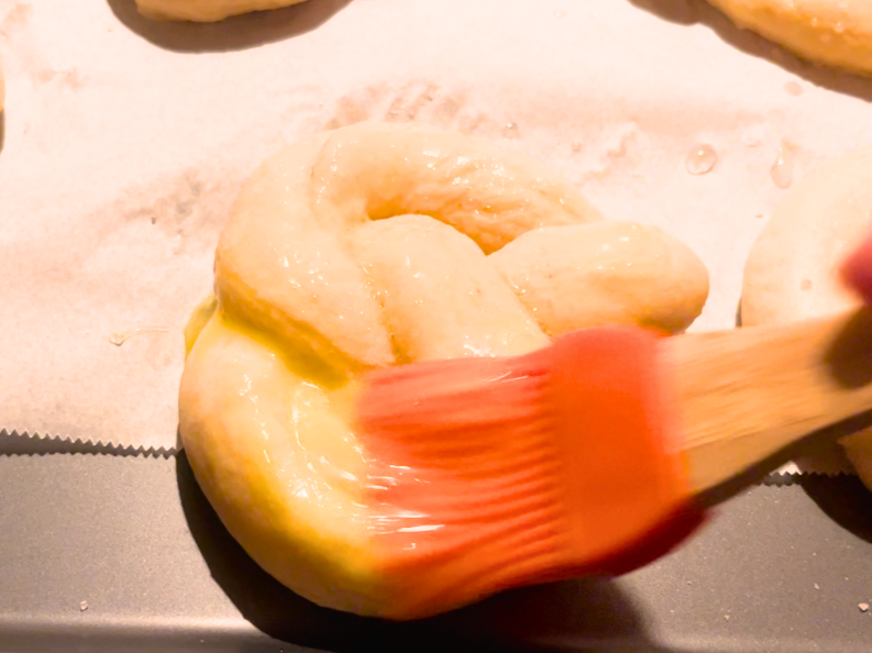 Woman brushing a boiled pretzel with an egg washing 
