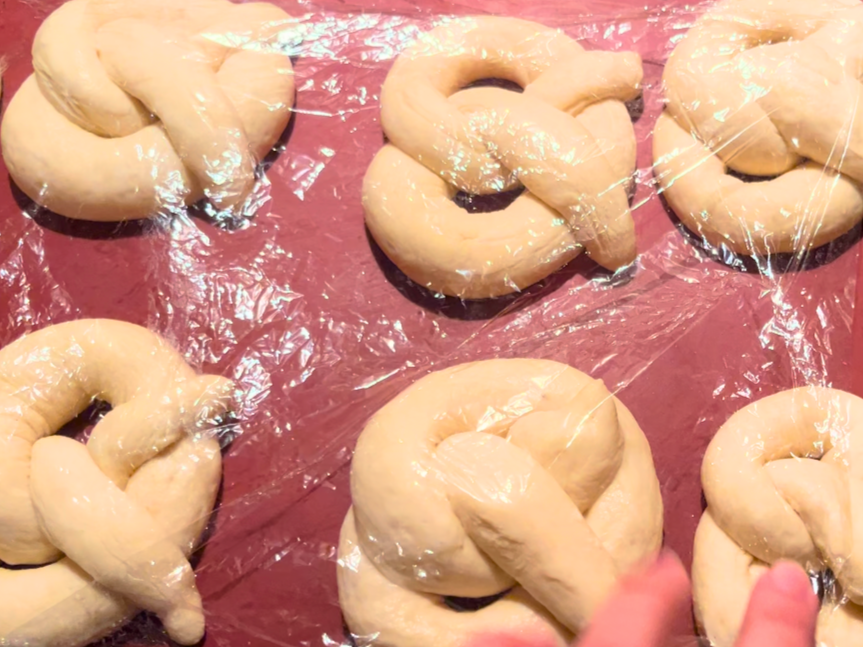 Risen pretzels covered in cling-film on a red silicone mat