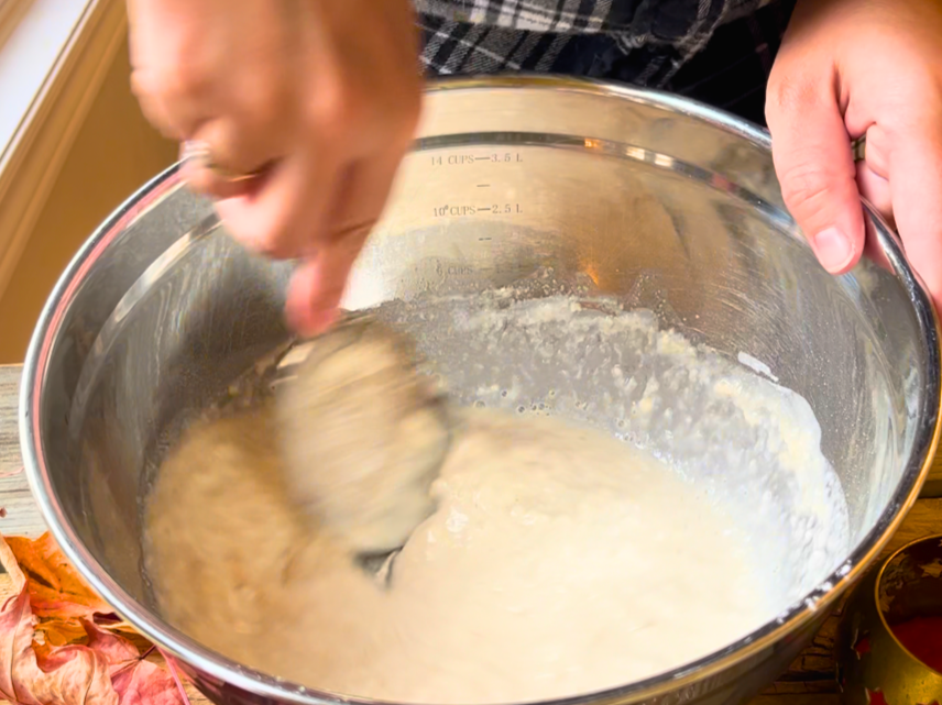 Woman mixing pretzel dough in a large metal bowl.