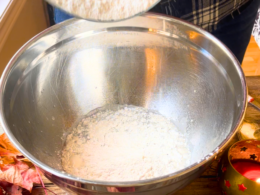 Woman adding flour to a metal bowl.