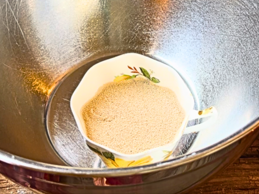 A large metal bowl with a small cup of warm water, sugar, and yeast.