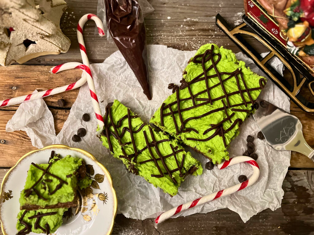 No bake chocolate mint bars on parchment paper with three candy canes and a piping bag in the background