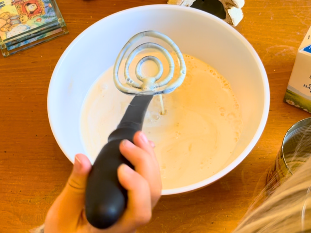 Child stirring a bowl with a milk mixture for a tres leches cake, in a large porcelain bowl.