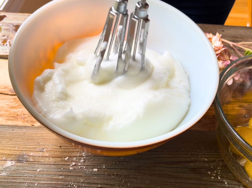 woman beating egg whites in a porcelain bowl with a rotary beater.