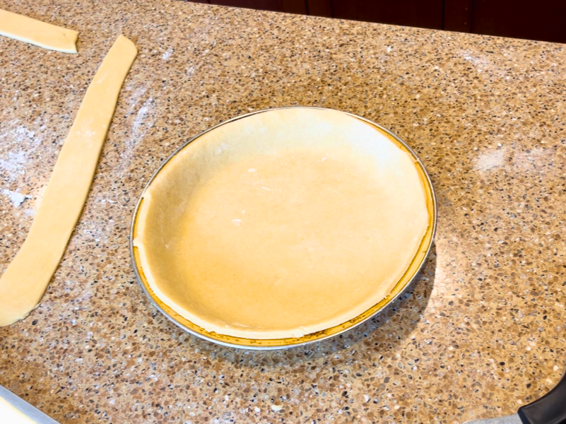 An un baked pie crust on a brown counter top.