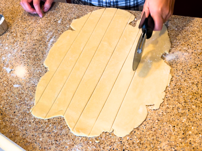 A woman cutting pie dough with a pizza cutter.