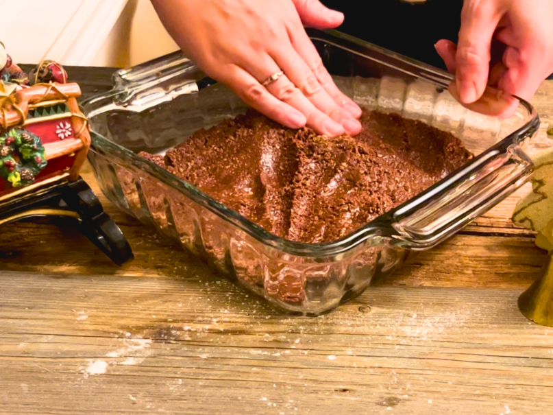 Woman pressing the chocolate base into an 8 in. square casserole dish.