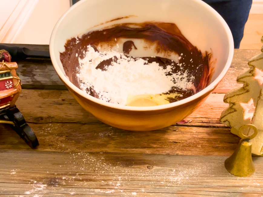 A large bowl with melted chocolate, icing sugar, and an egg.