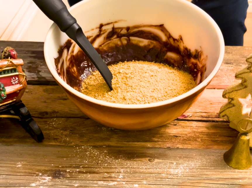 Woman adding graham cracker crumbs to a bowl with a chocolate mixture in it. 