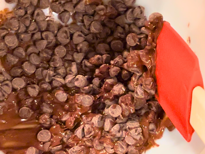 A white bowl with melting chocolate chips and a white and red spatula.