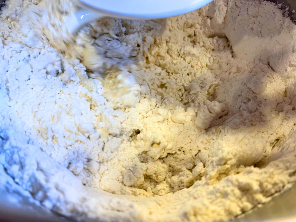 A bread dough mixture in the bowl of a stand mixer with the dough hook attachment