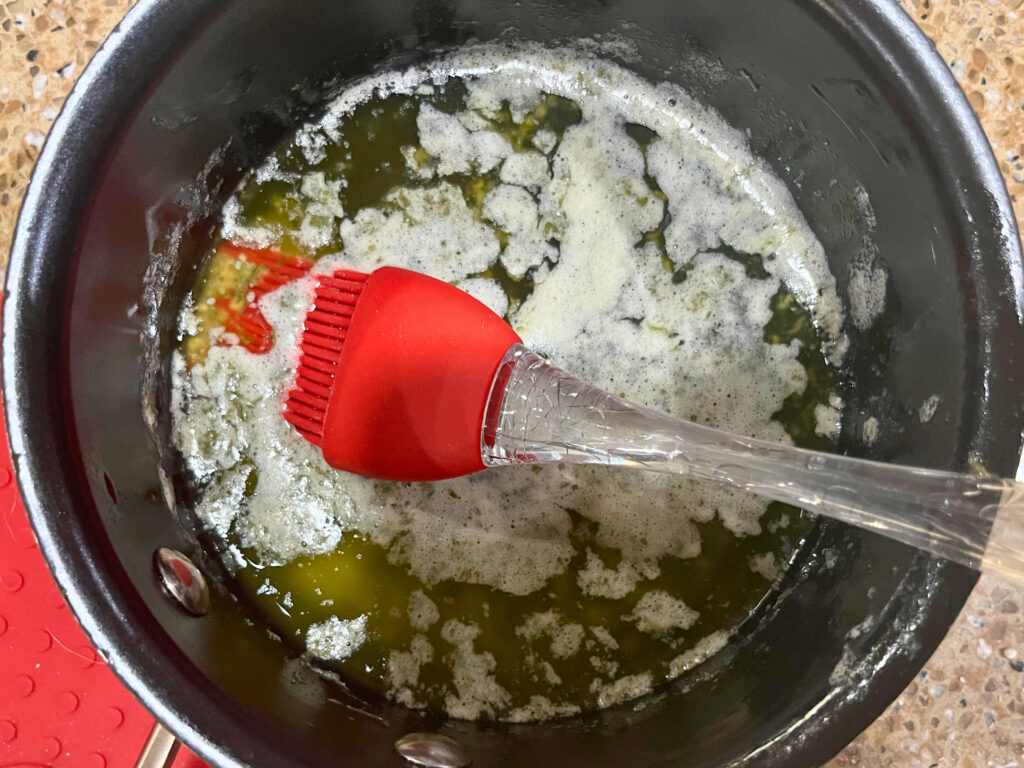 A sauce pot with melted butter mixture. A red silicone brush inside.