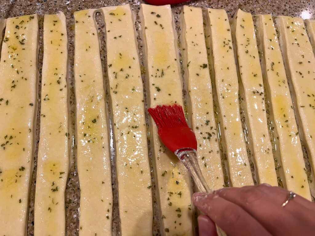 Woman brushing strips of dough with a garlic butter mixture.