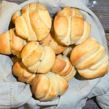 A basket of pull apart garlic dinner rolls with a grey napkin on a wooden table.