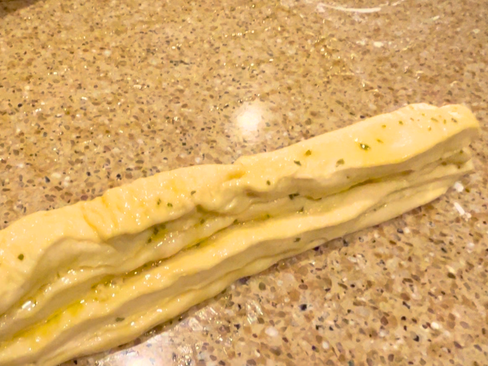 A stack of 4 strips of dough with garlic butter brushed in between the strips.