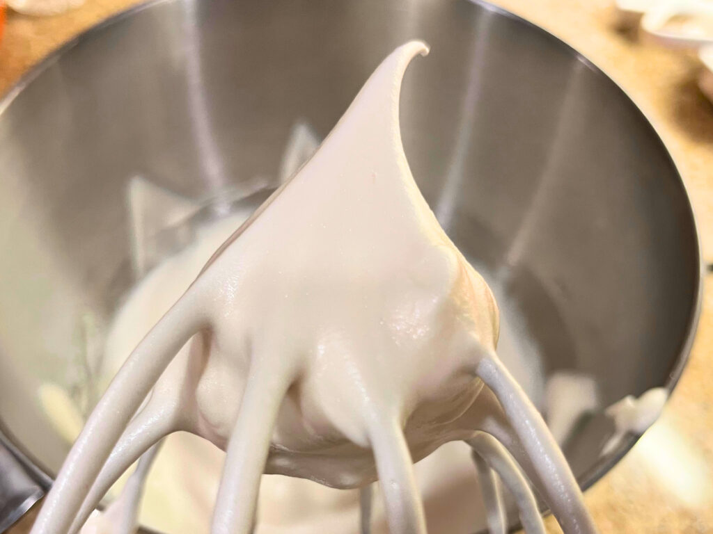 A whisk attachment with a egg white meringue stiff peak at the tip.