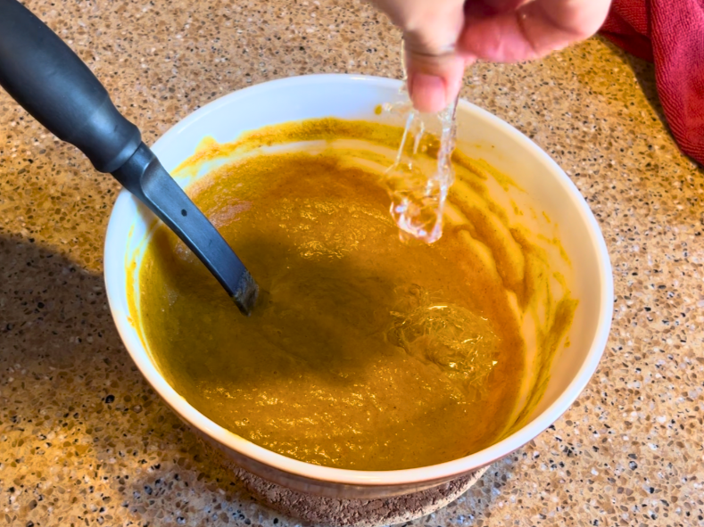 Woman dropping a softened gelatine leaf in to a bowl of pumpkin pie filling.