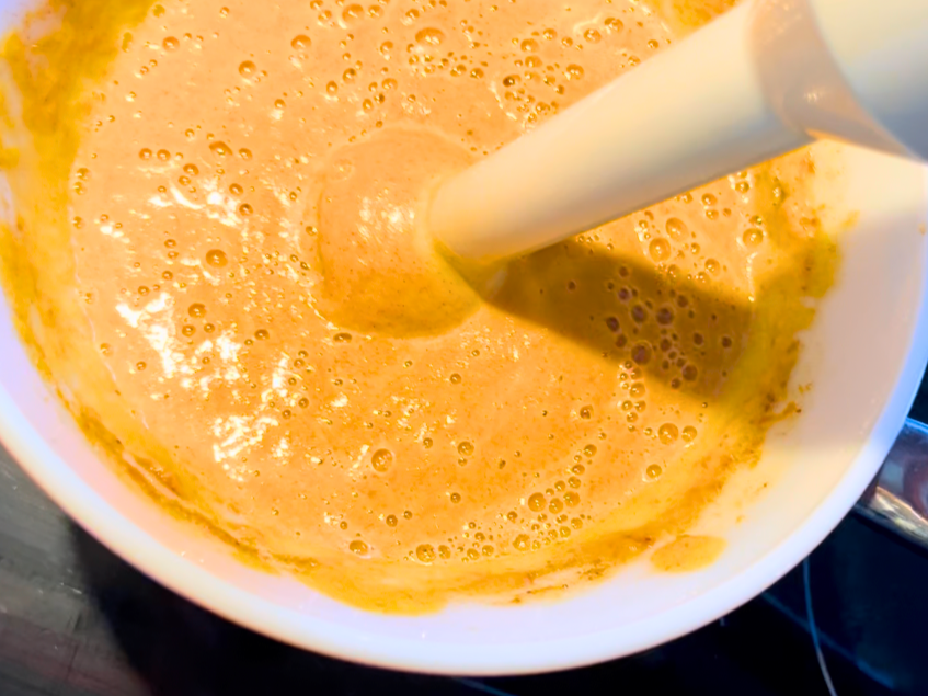 Woman using an immersion blender to puree pumpkin pie filling.