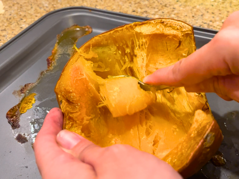 Woman removing the cooked flesh from a cooked pie pumpkin