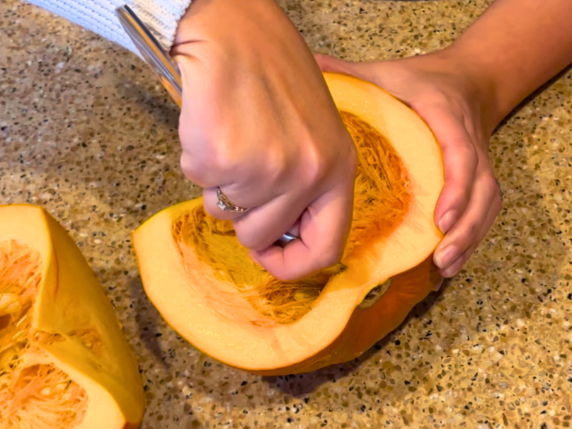 Woman removing the seeded area from a small pie pumpkin with a large spoon.