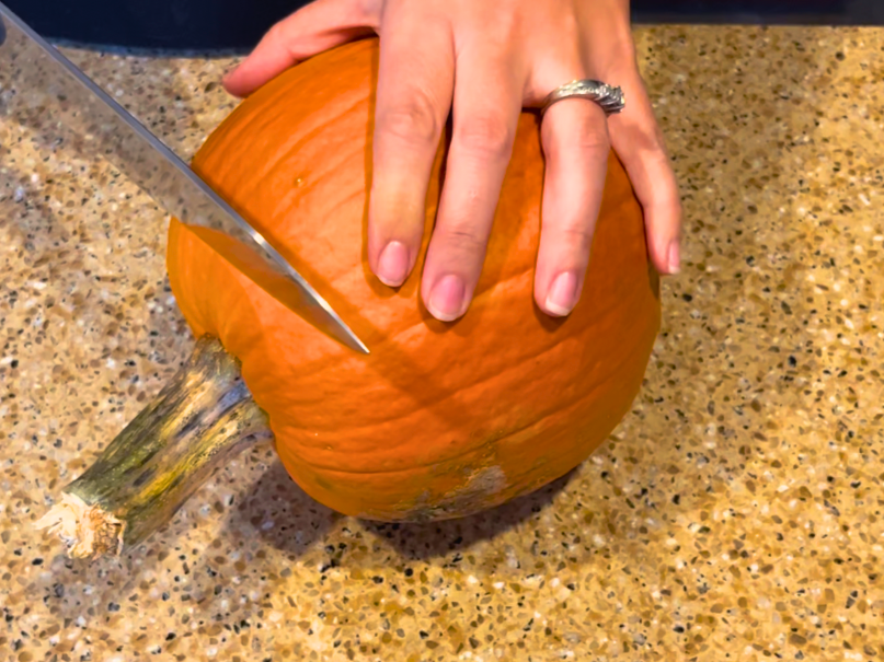 Woman cutting the top off of a small pie pumpkin.