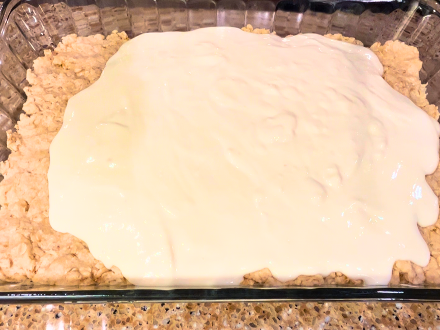 A baked oatmeal crust with a cheesecake layer being poured on top