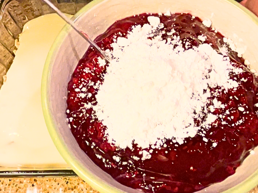 A white bowl with cranberry sauce and cornstarch on top