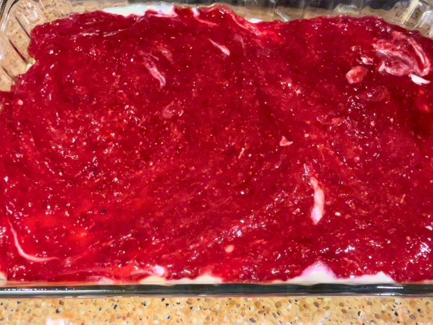 An uncooked cheesecake bar with cranberry sauce spread over top.