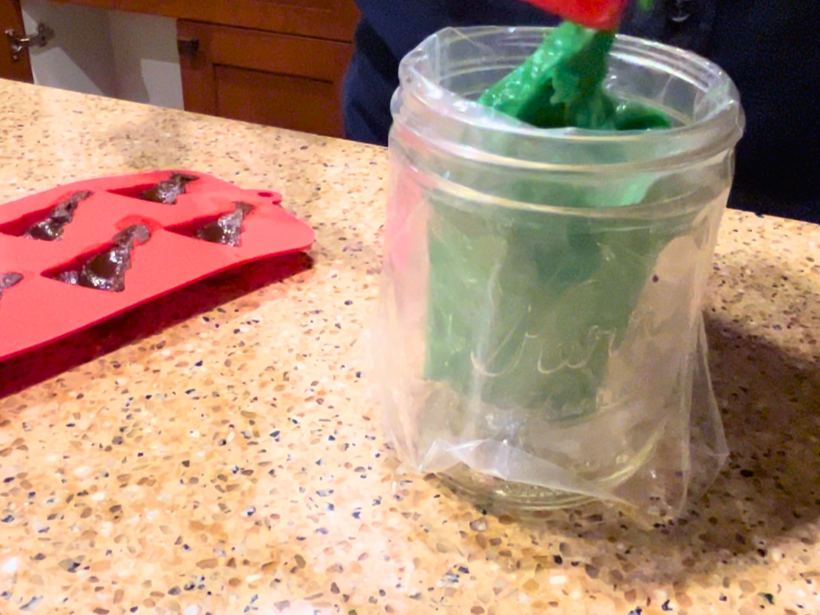 Woman putting melted mint chips into a piping bag resting in a mason jar.