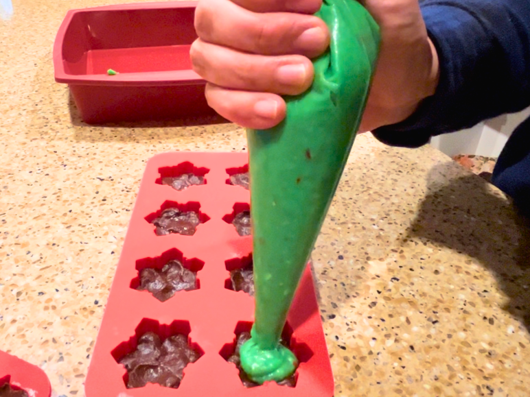 Woman piping a green melted chocolate mixture into snowflake silicone molds.