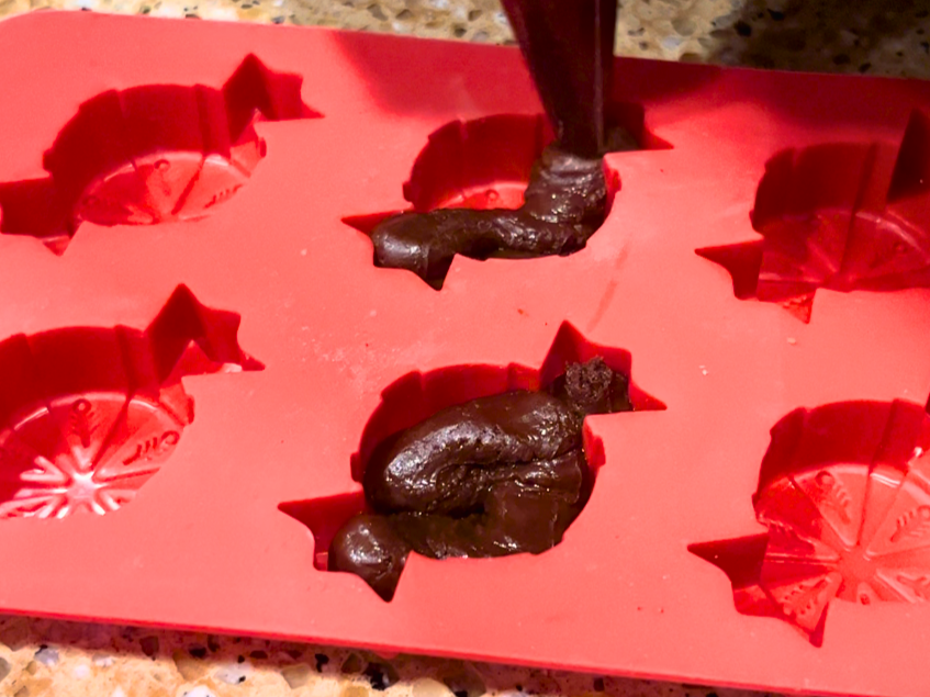 Woman piping melted chocolate mixture into candy shaped silicone molds.