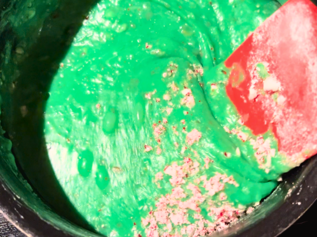 A pot with green tinted melted white chocolate chips and crushed candy cane pieces.