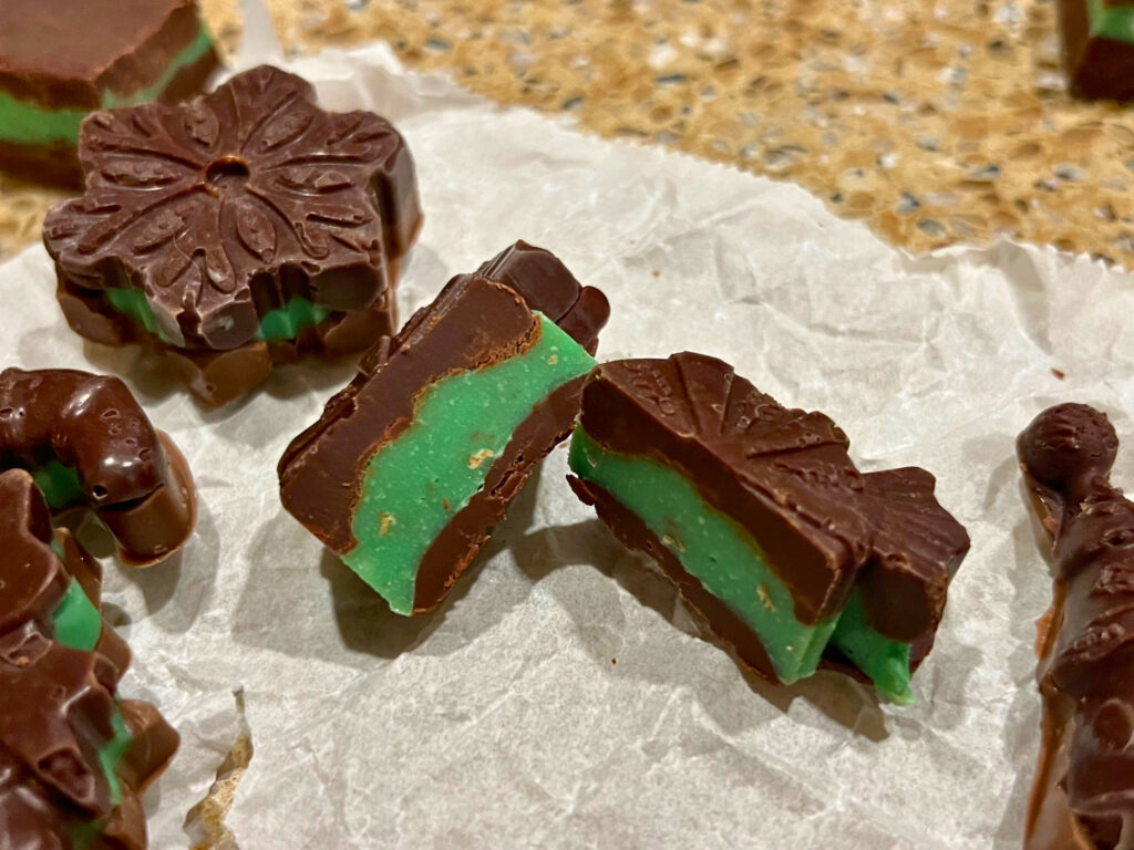 Chocolate mint candies molded in Christmas designs on a piece of parchment paper.