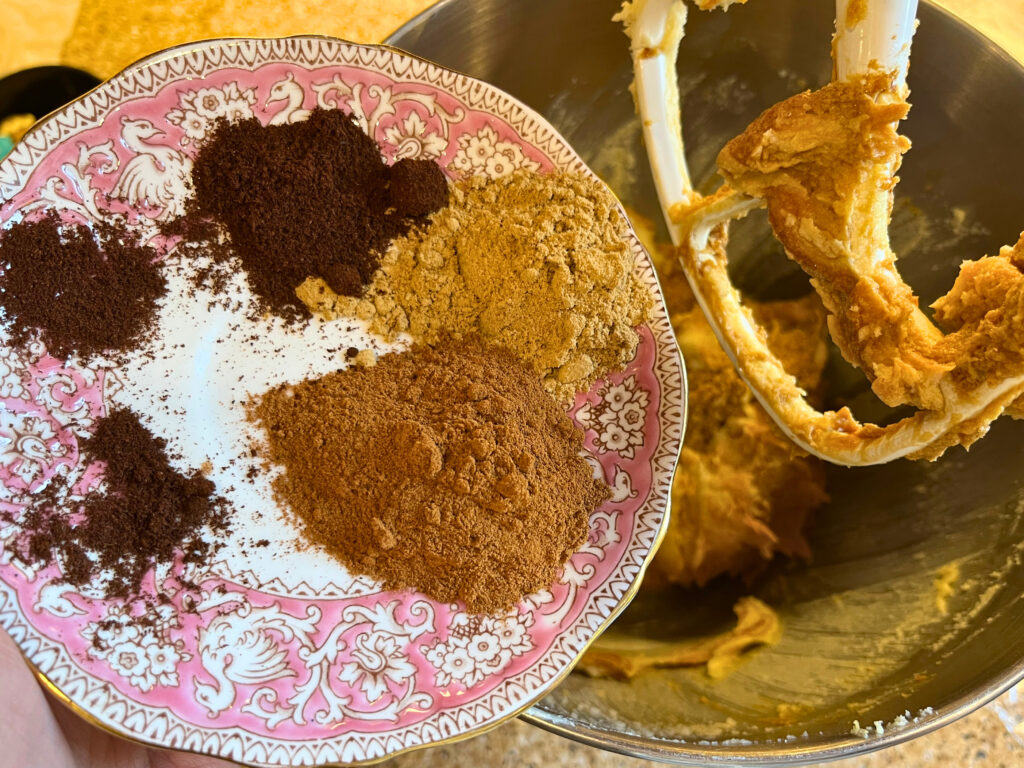 A pink and white plate with cinnamon, ground ginger, and clove on it.
