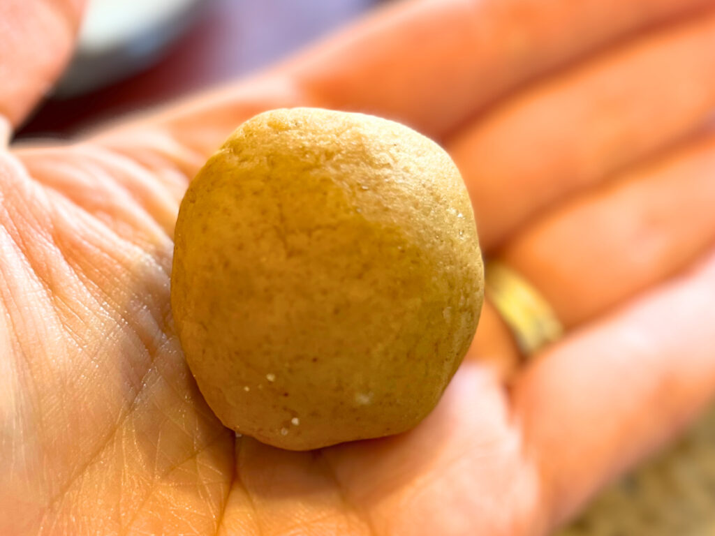 Woman holding a rolled ball of gingerbread cookie dough in her palm.
