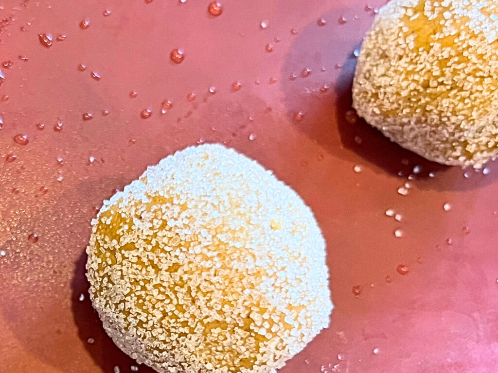 Balls of gingerbread cookie dough on a red baking mat. The cookie dough is dusted in white sugar.