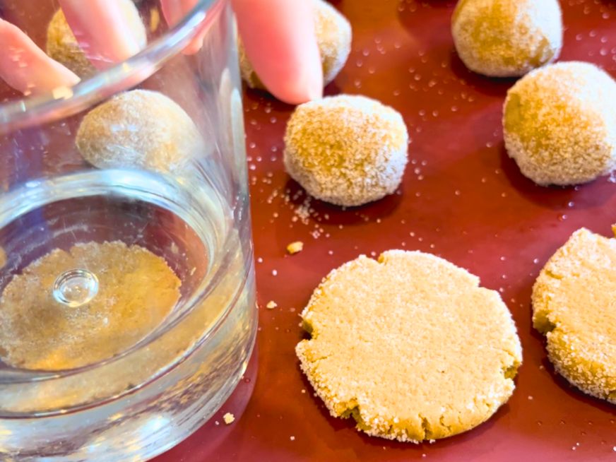 A woman pressing dough balls into a cookie shape with a glass.