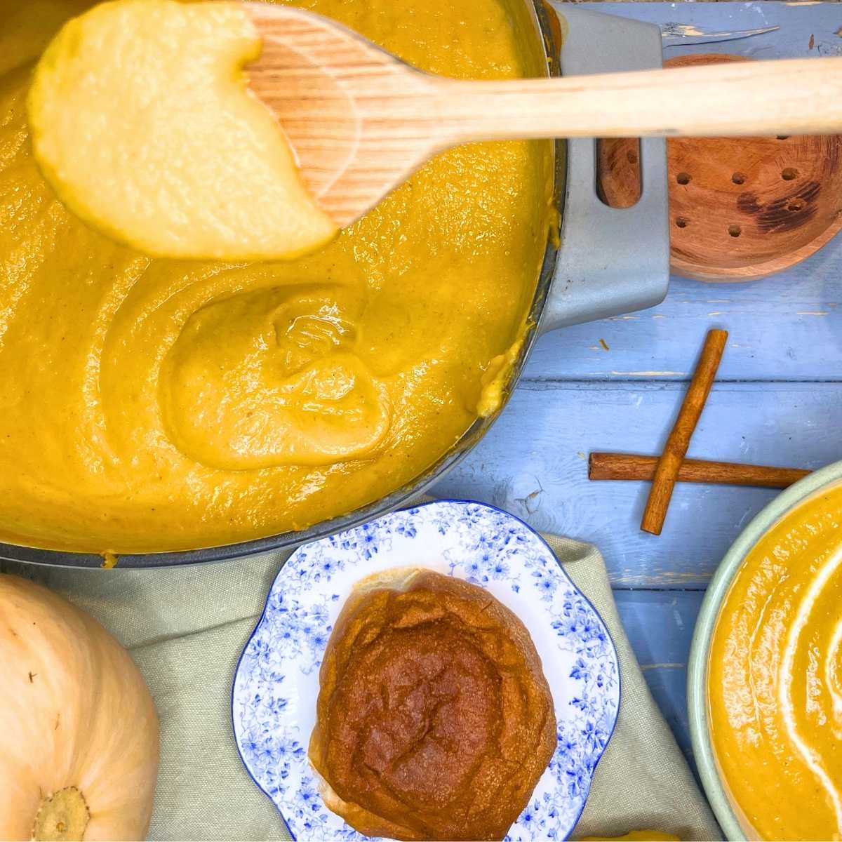 A large pot of butternut squash soup. A woman is holding a wooden spoon with soup on it.