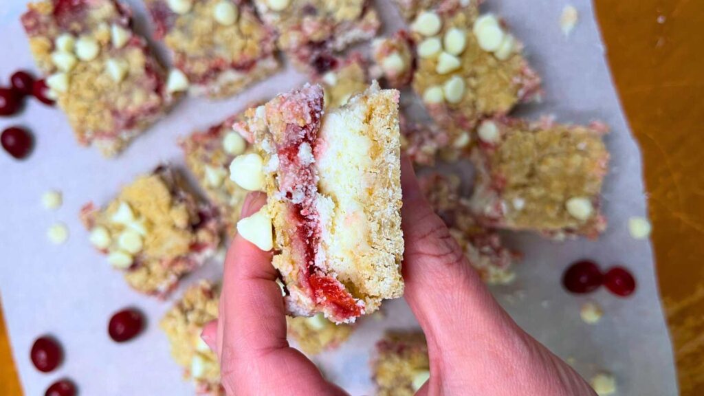 A woman is holding a cranberry cheesecake bar. There are more in the background.