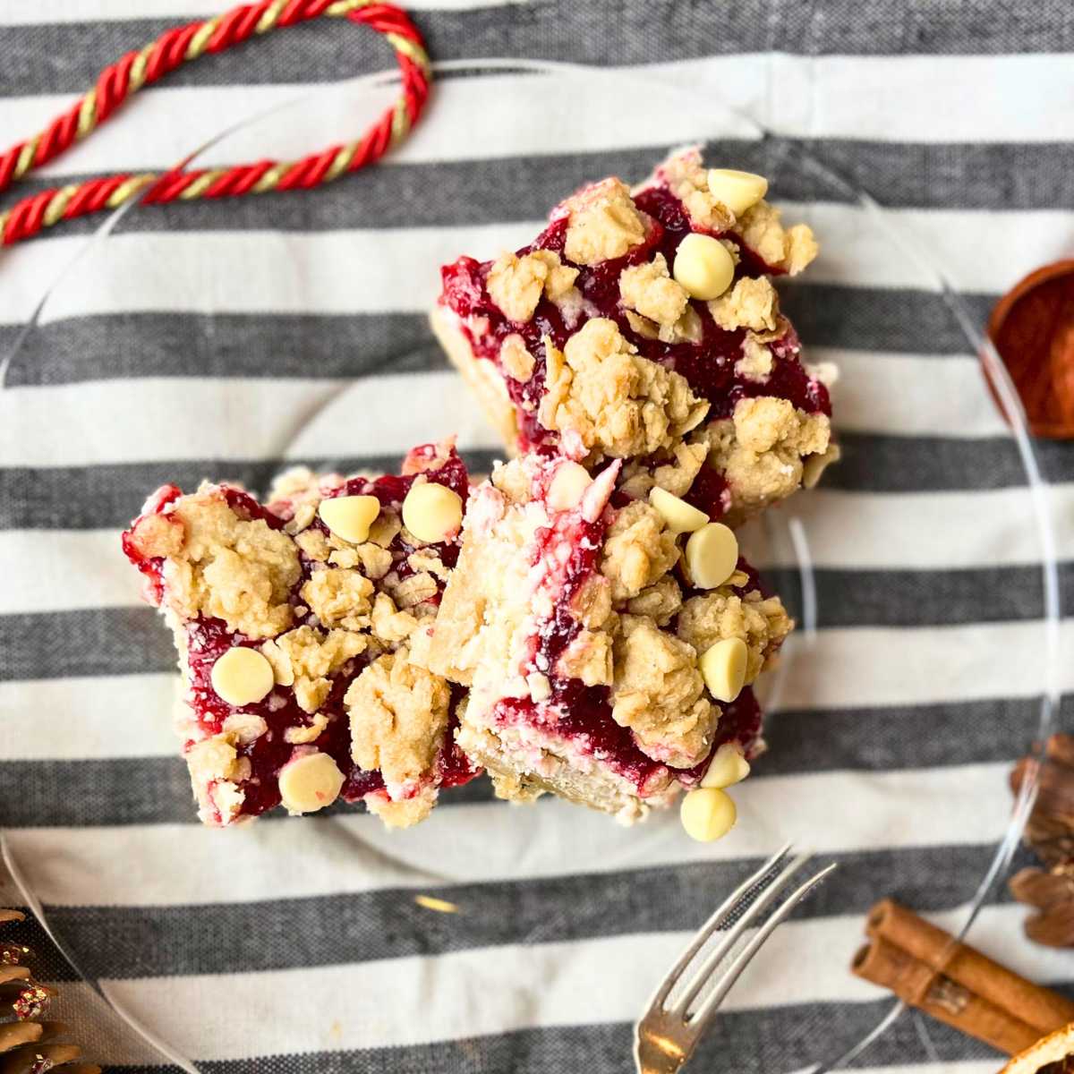 There cranberry cheesecake squares on a glass plate on a grey and white cloth.