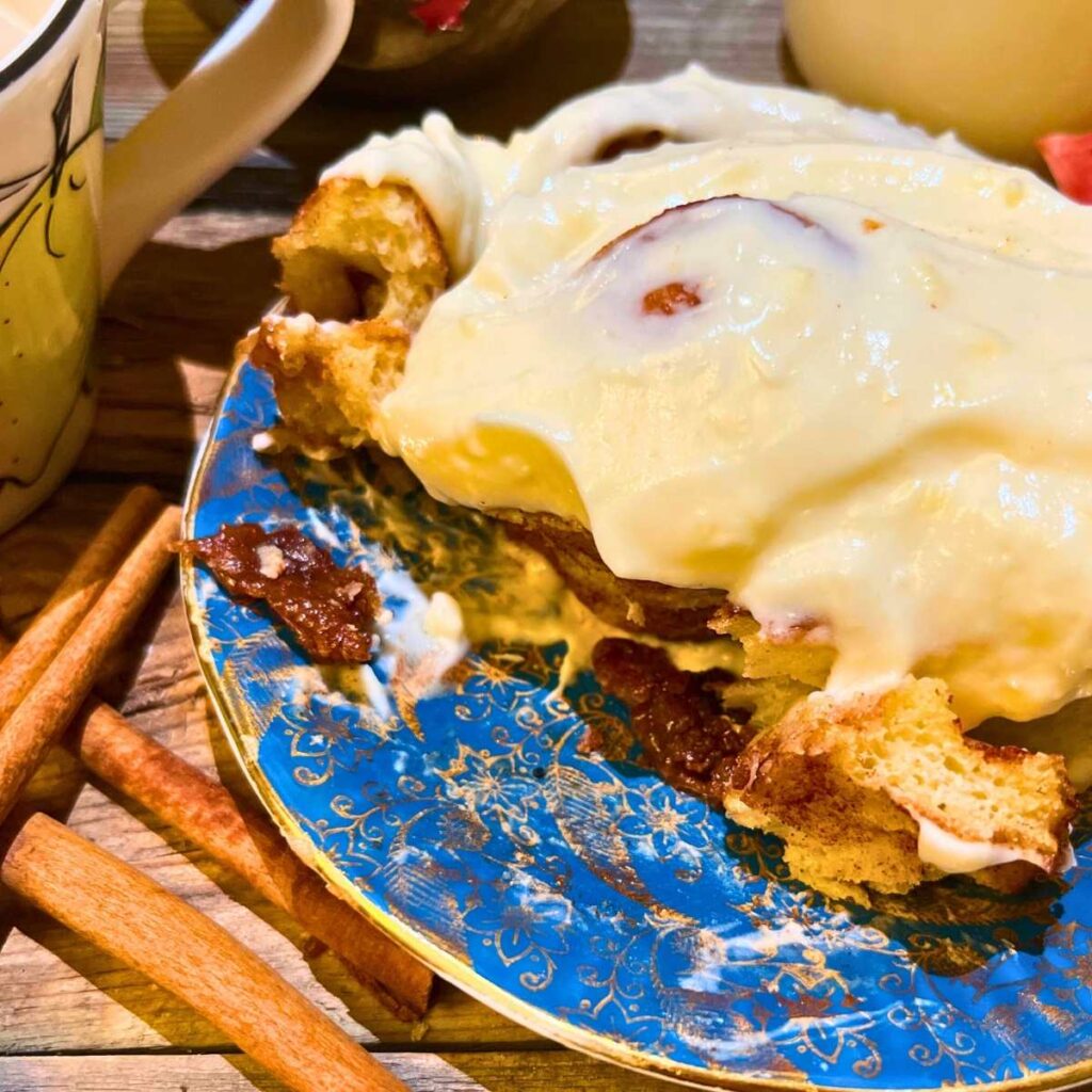 A cinnamon roll with cream cheese icing on a blue plate.