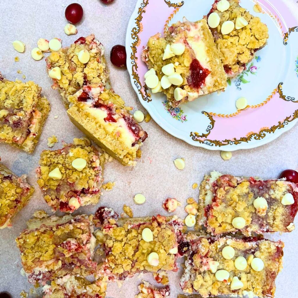 An arrangement of cranberry cheesecake bars on a table. Some are on a pink floral plate.